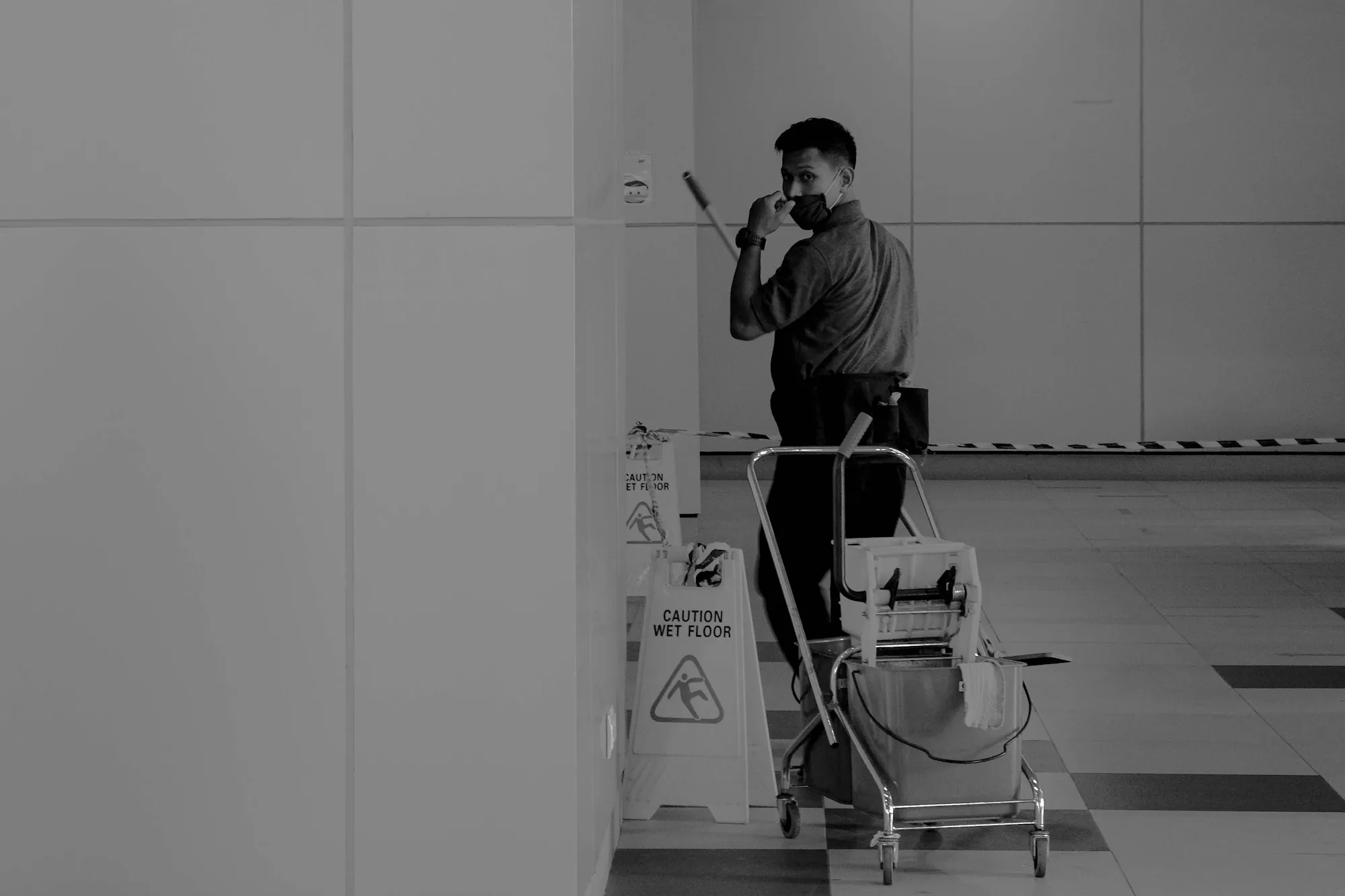 Janitor with a cleaning cart in a white corridor